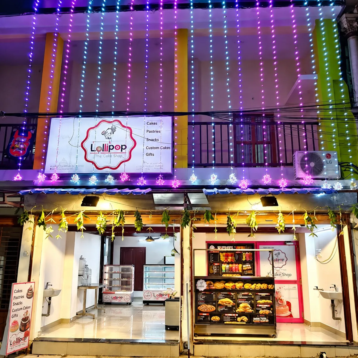 Lollipop The Cake Shop storefront in Trichy, lit with festive string lights at night